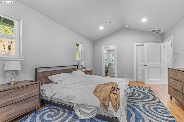 bedroom featuring lofted ceiling, ensuite bathroom, and light wood-type flooring