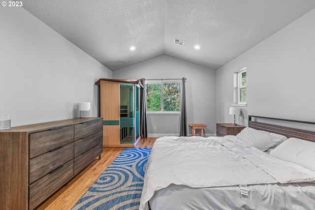 bedroom featuring multiple windows, lofted ceiling, light hardwood / wood-style flooring, and a textured ceiling