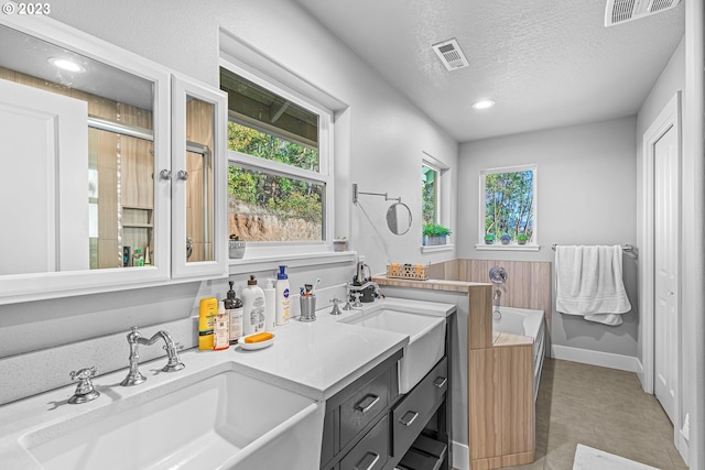 bathroom with large vanity, a washtub, a textured ceiling, dual sinks, and tile floors