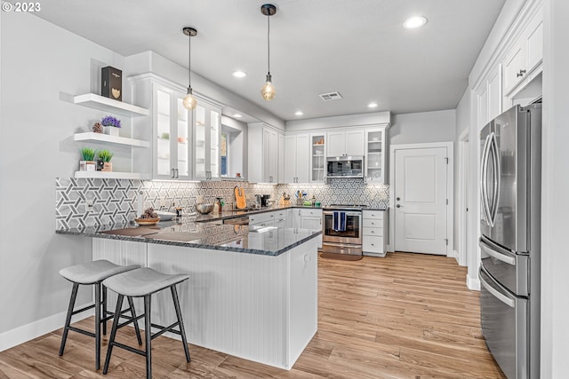 kitchen featuring stainless steel appliances, kitchen peninsula, tasteful backsplash, light hardwood / wood-style flooring, and hanging light fixtures