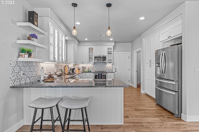 kitchen featuring appliances with stainless steel finishes, white cabinetry, kitchen peninsula, light hardwood / wood-style flooring, and hanging light fixtures