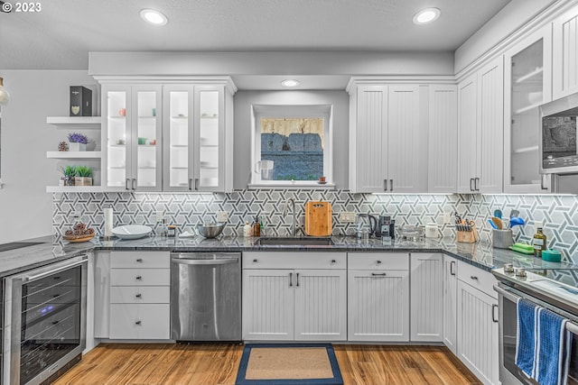 kitchen with appliances with stainless steel finishes, tasteful backsplash, light hardwood / wood-style floors, white cabinets, and wine cooler