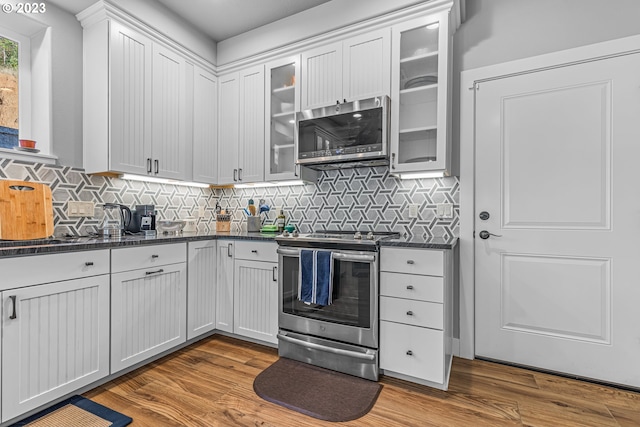 kitchen featuring white cabinetry, light hardwood / wood-style flooring, stainless steel appliances, dark stone counters, and tasteful backsplash