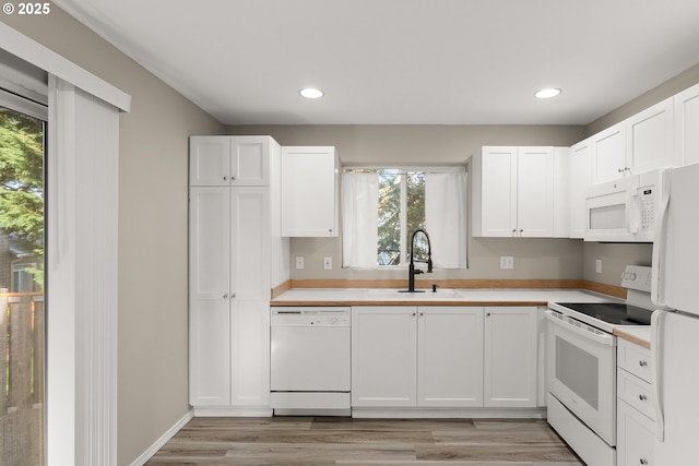 kitchen with white cabinetry, sink, white appliances, and light hardwood / wood-style floors