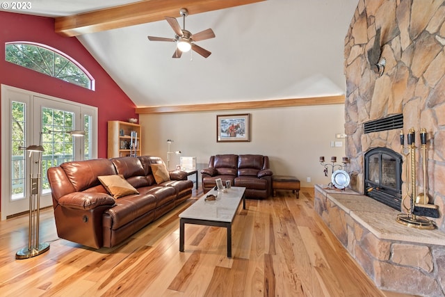 living room with ceiling fan, beamed ceiling, light hardwood / wood-style floors, high vaulted ceiling, and a stone fireplace