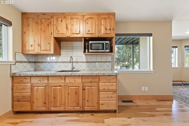 kitchen with light wood-type flooring, a wealth of natural light, tasteful backsplash, and sink