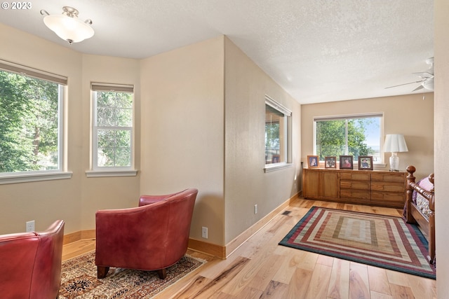 living area featuring a textured ceiling, ceiling fan, and light hardwood / wood-style flooring