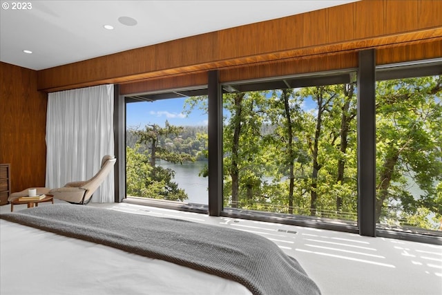 unfurnished bedroom with carpet, a water view, wood walls, and multiple windows