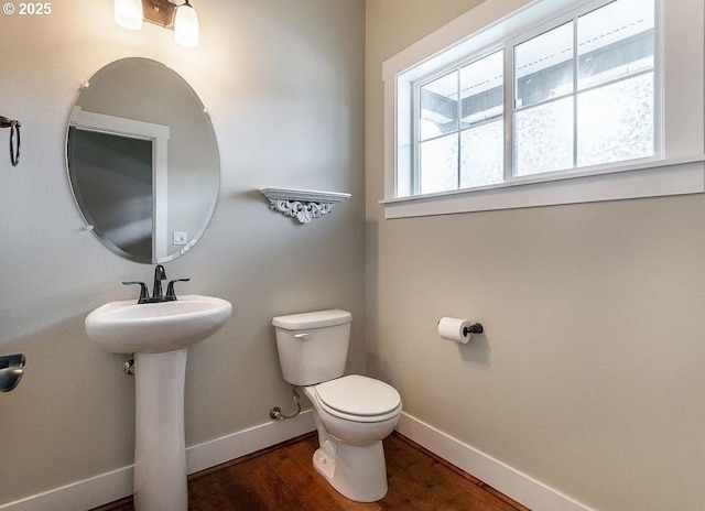 half bathroom with baseboards, toilet, healthy amount of natural light, and wood finished floors