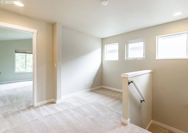 unfurnished room with carpet, healthy amount of natural light, a textured ceiling, and baseboards