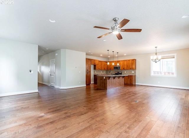 unfurnished living room featuring baseboards, ceiling fan, a chandelier, recessed lighting, and wood finished floors