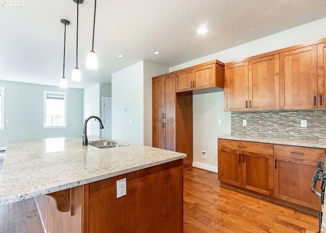 kitchen featuring a sink, brown cabinets, light stone counters, backsplash, and a textured ceiling