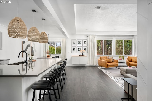 kitchen featuring dark wood-style floors, decorative light fixtures, a sink, a textured ceiling, and a kitchen bar