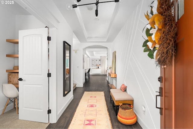 hall featuring arched walkways, a tray ceiling, dark wood-type flooring, and baseboards