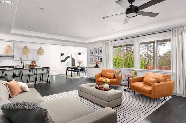 living room featuring ornamental molding, ceiling fan, a tray ceiling, and dark wood-type flooring