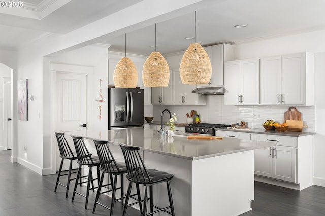 kitchen featuring stainless steel gas stove, tasteful backsplash, crown molding, under cabinet range hood, and refrigerator with ice dispenser