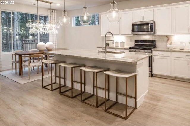 kitchen with pendant lighting, sink, stainless steel appliances, an island with sink, and white cabinets