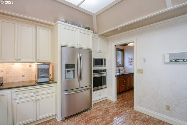 kitchen with dark stone countertops, white cabinetry, backsplash, and stainless steel appliances