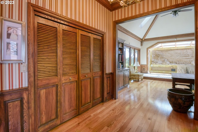 hall featuring light hardwood / wood-style flooring, a notable chandelier, ornamental molding, and high vaulted ceiling