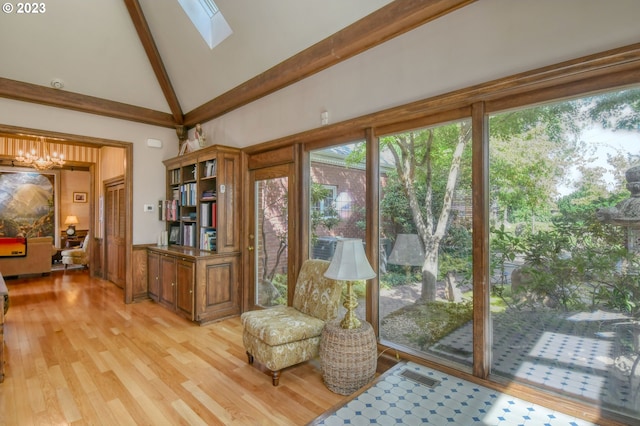 sitting room with a skylight, a notable chandelier, high vaulted ceiling, and light wood-type flooring