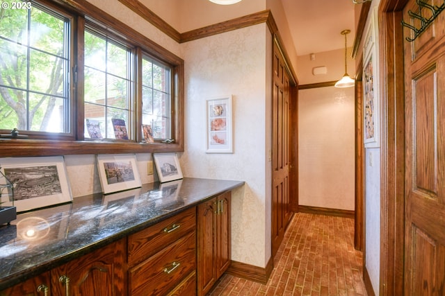 interior space with crown molding, hanging light fixtures, dark stone countertops, and a healthy amount of sunlight