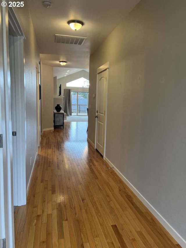 hall featuring visible vents, baseboards, and hardwood / wood-style flooring