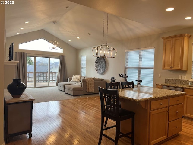 kitchen with lofted ceiling, wood-type flooring, open floor plan, light stone countertops, and a kitchen bar