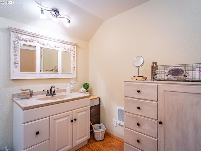 bathroom with wood-type flooring, vaulted ceiling, and vanity