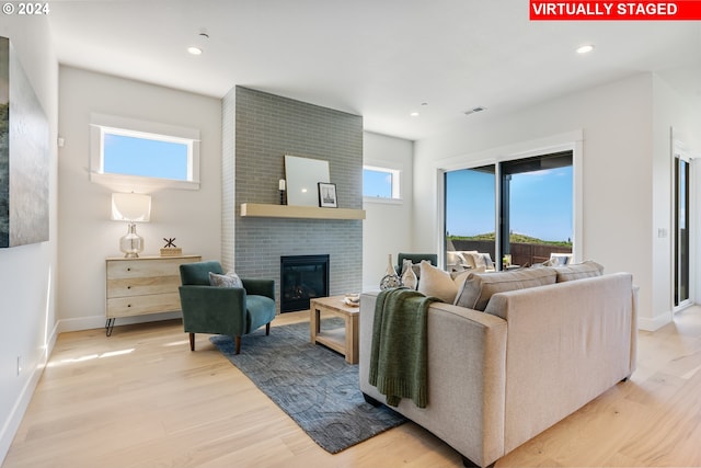 living room featuring a brick fireplace, plenty of natural light, and light wood-type flooring