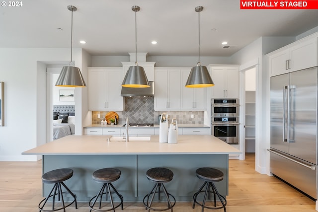 kitchen featuring a kitchen bar, white cabinetry, hanging light fixtures, a center island with sink, and appliances with stainless steel finishes