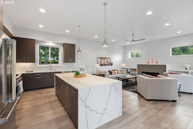 kitchen with a center island, ceiling fan, a fireplace, light hardwood / wood-style flooring, and light stone countertops