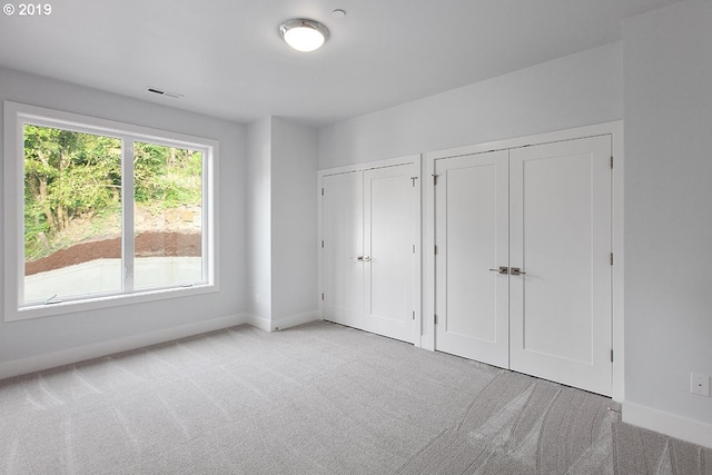 unfurnished bedroom featuring light colored carpet and multiple closets