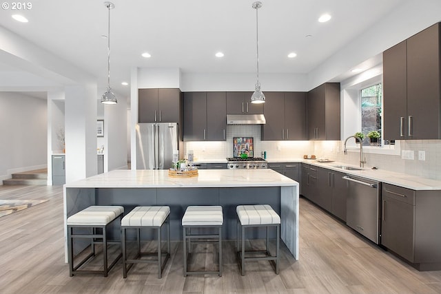 kitchen featuring decorative light fixtures, appliances with stainless steel finishes, light wood-type flooring, a kitchen island, and tasteful backsplash