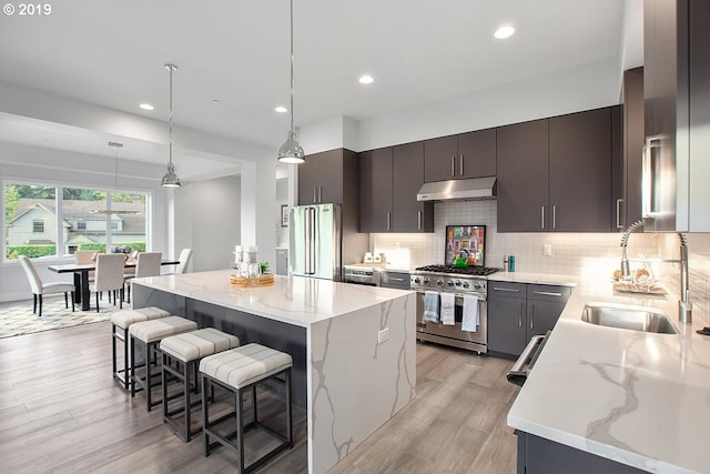 kitchen with light stone counters, hanging light fixtures, light hardwood / wood-style flooring, premium appliances, and a center island