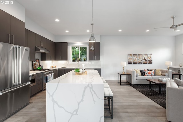 kitchen with ceiling fan, light hardwood / wood-style flooring, high end appliances, tasteful backsplash, and a center island