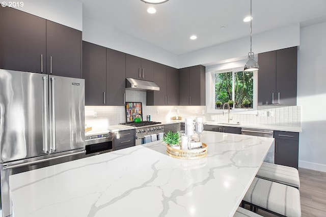 kitchen with backsplash, appliances with stainless steel finishes, light stone countertops, and pendant lighting