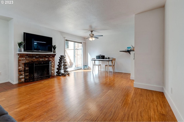 living room featuring a brick fireplace, a textured ceiling, ceiling fan, and light wood-type flooring