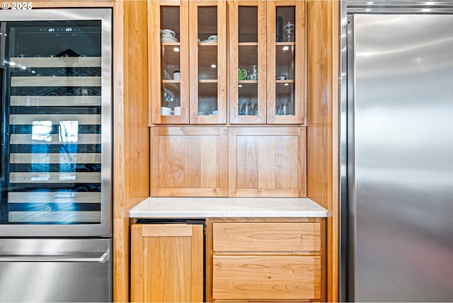 interior space featuring stainless steel refrigerator, beverage cooler, glass insert cabinets, and light countertops