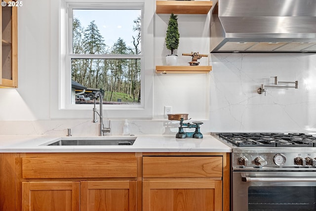 kitchen featuring wall chimney exhaust hood, high end stove, a sink, backsplash, and healthy amount of natural light