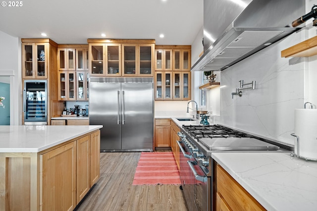 kitchen with high end appliances, wall chimney exhaust hood, beverage cooler, light wood finished floors, and a sink