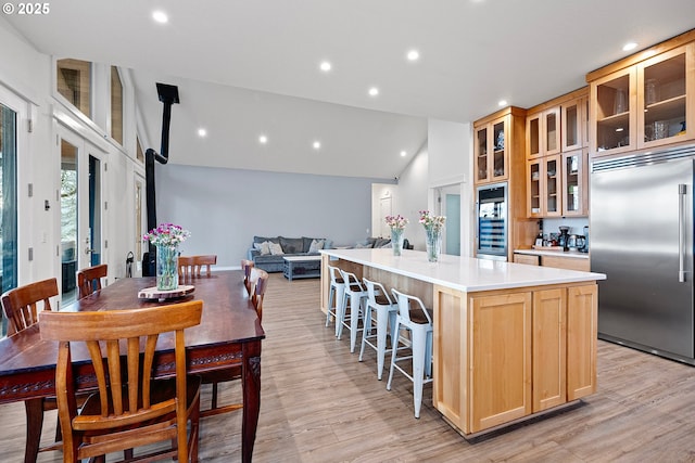 kitchen with built in fridge, light wood-style flooring, a center island with sink, light countertops, and light brown cabinets