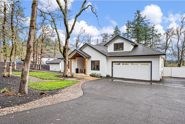 view of front facade featuring asphalt driveway, a shingled roof, and fence