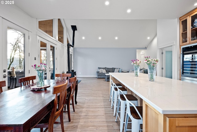dining space with light wood-style flooring, a wood stove, recessed lighting, and high vaulted ceiling