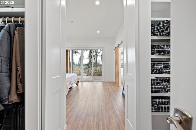 hallway featuring wood finished floors, recessed lighting, baseboards, and a barn door