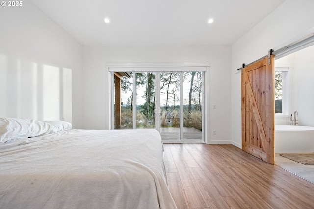 unfurnished bedroom with a barn door, light hardwood / wood-style floors, and access to exterior