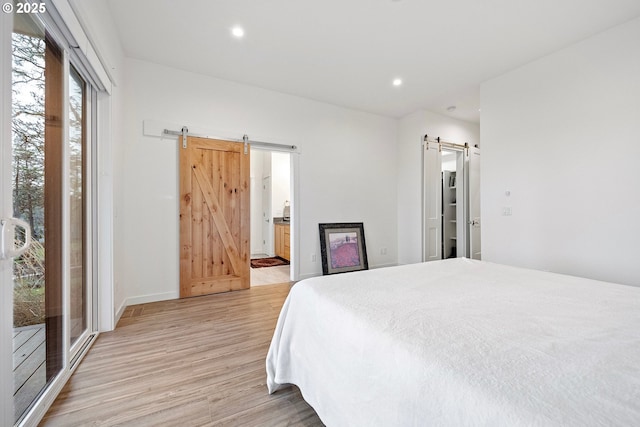 bedroom with a barn door, light wood-style flooring, recessed lighting, ensuite bath, and baseboards