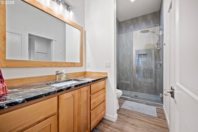 bathroom with toilet, a stall shower, vanity, and wood finished floors