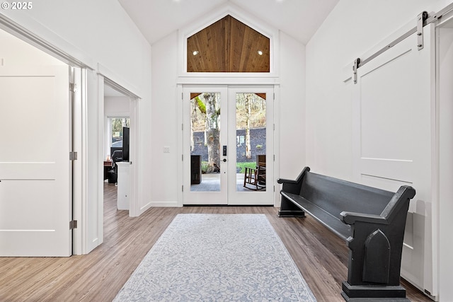 interior space with a barn door, light hardwood / wood-style floors, high vaulted ceiling, and french doors