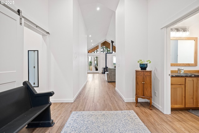 hallway featuring light wood-style flooring, high vaulted ceiling, a sink, a barn door, and baseboards