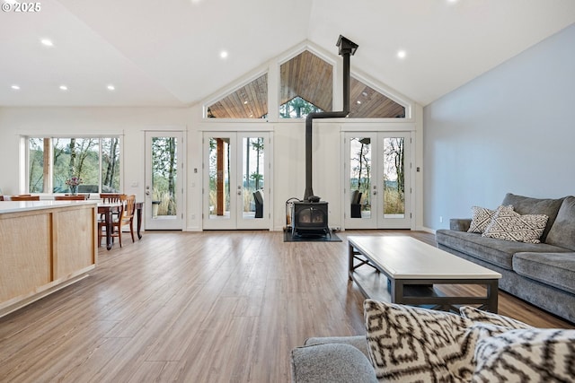 living area featuring a wood stove, french doors, light wood-style flooring, recessed lighting, and high vaulted ceiling